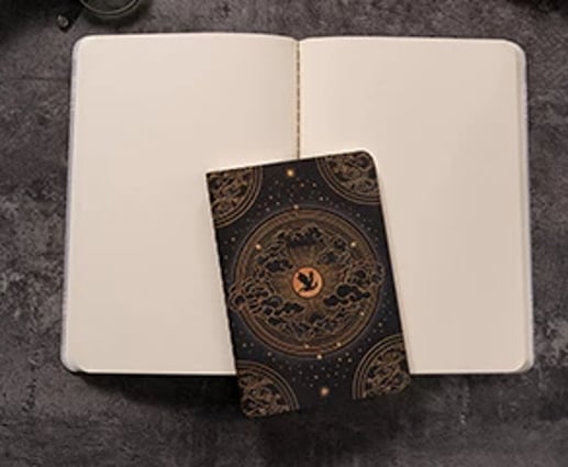 A white open book cahier with another smaller format cahier closed on top.